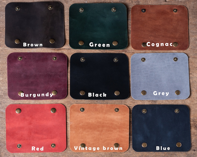 May include: Nine leather swatches in different colours, including brown, green, cognac, burgundy, black, grey, red, vintage brown, and blue. Each swatch has two brass rivets on the top and bottom.
