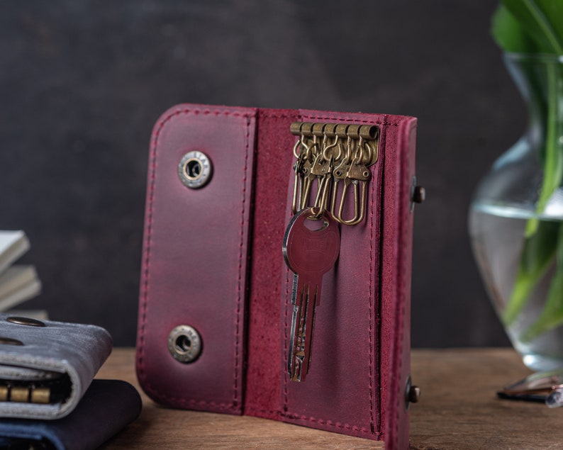 May include: A burgundy leather key holder with a key ring and a key inside. The key holder has a flap that closes with a snap.