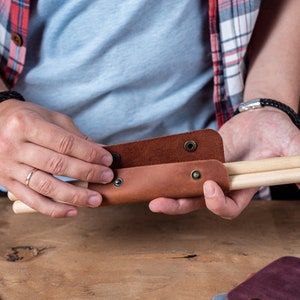 May include: A brown leather case with poppers, holding two wooden drumsticks.