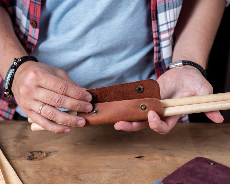 May include: A brown leather case with poppers, holding two wooden drumsticks.