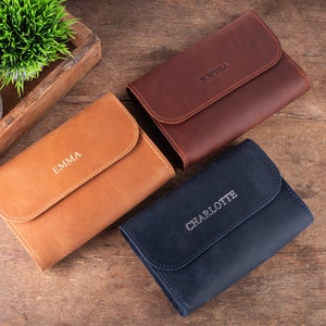 Op de afbeelding: Drie leren etui's in verschillende kleuren, elk met een naam erop gegraveerd: Emma, Sophia en Charlotte.