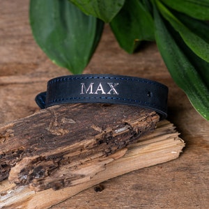 May include: A dark blue leather dog collar with white stitching and the name "MAX" engraved in silver.