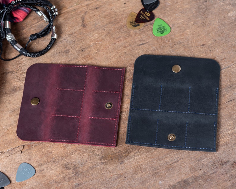 May include: Two leather guitar pick holders, one burgundy and one black, with multiple slots for picks and a snap closure.