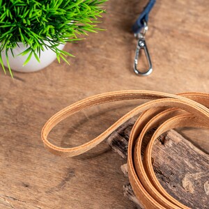 May include: A brown leather dog lead coiled on a wooden surface.