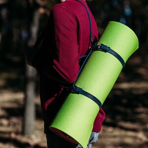 May include: A person wearing a red jumper carries a bright green yoga mat over their shoulder using a blue strap.