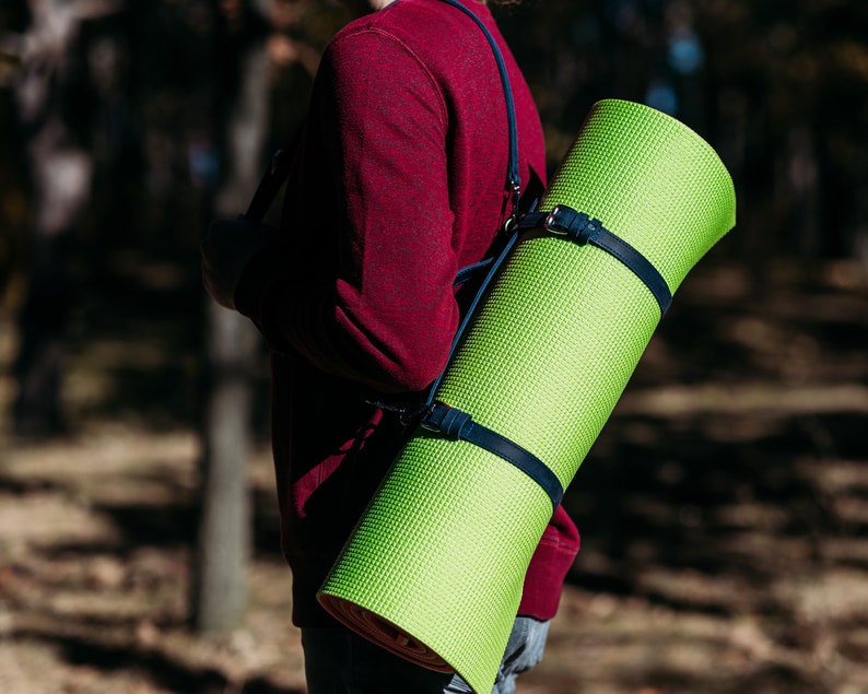 May include: A person wearing a red jumper carries a bright green yoga mat over their shoulder using a blue strap.