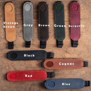 K&ouml;nnte beinhalten: Neun Leder-Kameragurtenden in verschiedenen Farben: Vintage Braun, Grau, Braun, Gr&uuml;n, Burgunder, Schwarz, Cognac, Rot und Blau. Jede Gurtenden hat ein rundes Loch in der Mitte.