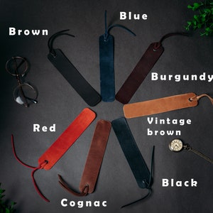 May include: A set of ten leather bookmarks in various colors, including brown, blue, burgundy, red, cognac, vintage brown, and black. The bookmarks are arranged in a circle on a dark gray surface.