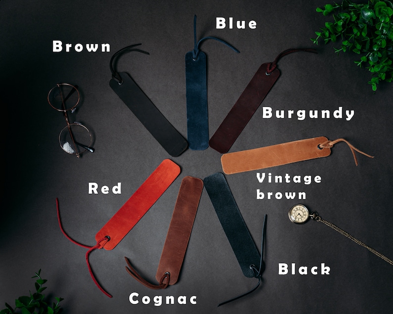 May include: A set of ten leather bookmarks in various colors, including brown, blue, burgundy, red, cognac, vintage brown, and black. The bookmarks are arranged in a circle on a dark gray surface.