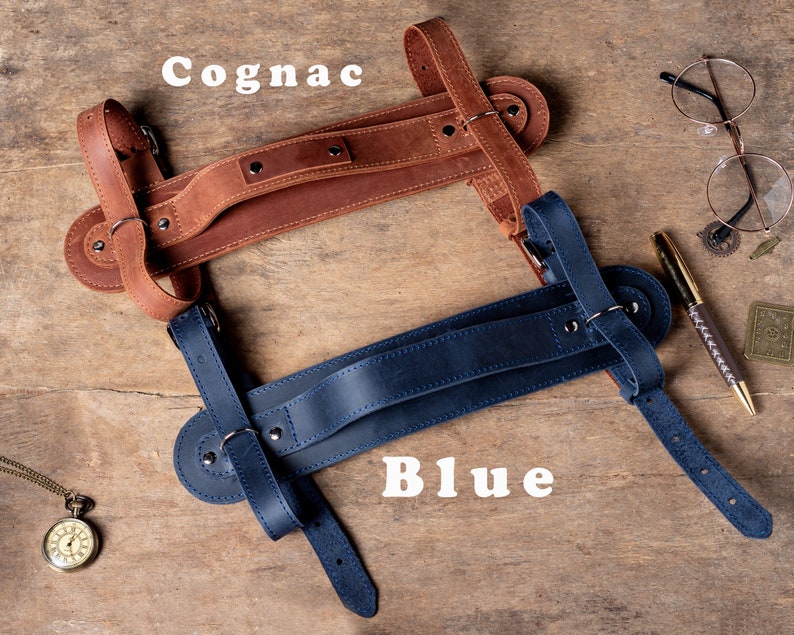 May include: Two leather camera straps, one brown and one blue, with adjustable straps and a handle. The straps are labelled "Cognac" and "Blue".