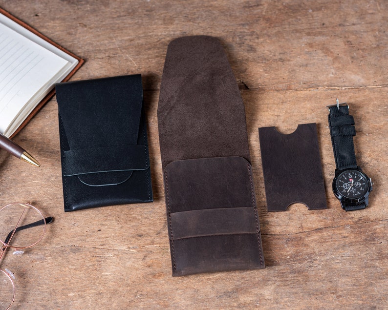 May include: A set of four leather pouches in brown and black. The pouches are made of a soft, supple leather and have a simple, elegant design. The pouches are perfect for storing small items like keys, wallets, or phones.