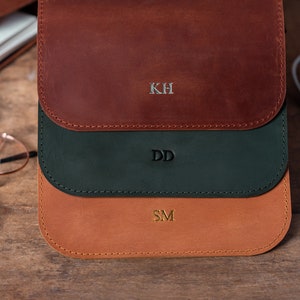Op de afbeelding: Drie leren etui's met verschillende kleuren leer en gepersonaliseerde initialen. De bovenste etui is van bruin leer met de initialen KH, de middelste etui is van groen leer met de initialen DD en de onderste etui is van bruin leer met de initialen SM.