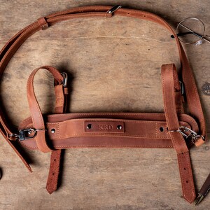 May include: A brown leather camera strap with adjustable straps and a buckle. The strap has the word "KRD" embossed on it.