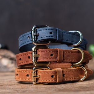May include: Three leather dog collars stacked on top of each other. The top collar is navy blue, the middle collar is brown, and the bottom collar is a lighter brown.