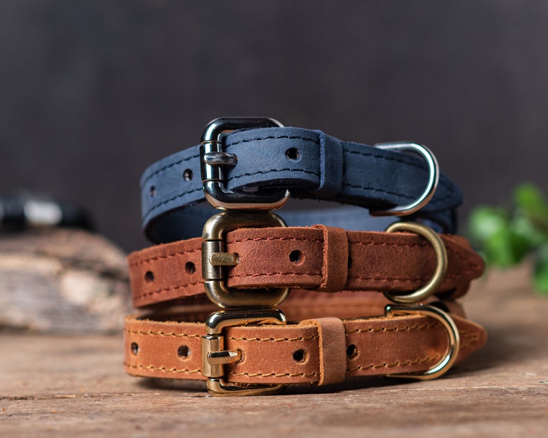 May include: Three leather dog collars stacked on top of each other. The top collar is navy blue, the middle collar is brown, and the bottom collar is a lighter brown.