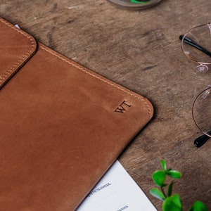 May include: A brown leather laptop sleeve with the initials "WT" embossed on the front.