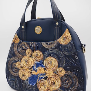 May include: A navy blue handbag with a top handle and a zipper closure. The bag features a print of a starry night sky with swirling yellow stars and a blue spaceship in the center.