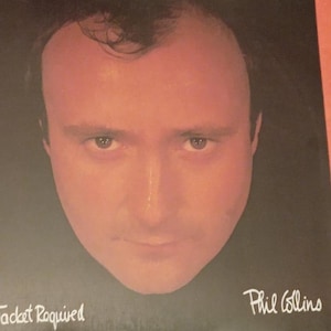 以下が含まれることがあります： 男性の顔のクローズアップが特徴のアルバムカバー。アルバムタイトル「...Jacket Required」は左下に白で印刷され、アーティスト名「Phil Collins」は右下にあります。背景は暗いです。
