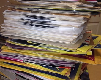 Puede incluir: Una pila de discos de vinilo vintage de varios colores, incluyendo negro, blanco, amarillo y rojo. Los discos están en sus fundas originales, algunas de las cuales están rasgadas o descoloridas. El texto "New Orthophonic High Fidelity" es visible en una de las fundas.