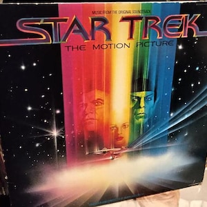May include: A vintage vinyl record cover for the Star Trek: The Motion Picture soundtrack. The cover features a colorful, abstract background with a spaceship and the faces of the main characters.