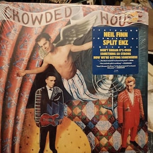 Op de afbeelding: Een vinyl platenhoes van de band "Crowded House" met Neil Finn, voorheen van Split Enz. De albumhoes toont een man met vleugels, een man in pak met een gitaar en een man in een rood pak. De albumtitel is "Crowded House" en het album bevat de nummers "Don't Dream It's Over", "Something So Strong" en "Now We're Getting Somewhere".