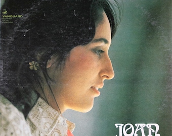 May include: A vintage vinyl record cover featuring a woman with long dark hair, wearing a white lace blouse. The cover is green and has the text "JOAN" in white, stylized lettering.