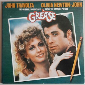 Può includere: Una copertina di un album in vinile vintage con John Travolta e Olivia Newton-John, le stelle del film musicale Grease. La copertina presenta uno sfondo verde con il titolo "Grease" in lettere bianche. Gli attori sono mostrati in un primo piano, con Travolta che indossa una giacca di pelle nera e Newton-John che indossa una camicia bianca.