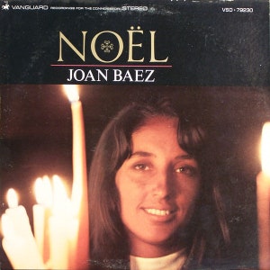 Puede incluir: Una portada de álbum de vinilo vintage con Joan Baez. El arte de la portada es un primer plano de la cara de Joan Baez, con velas en primer plano. El título del álbum "NOËL" está impreso en letras doradas grandes en la parte superior de la portada.