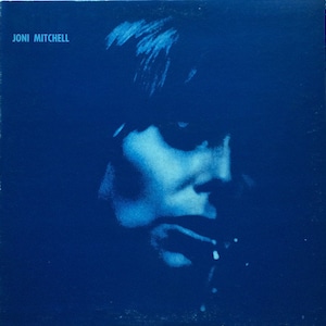 May include: A blue vinyl record album cover featuring a close-up of Joni Mitchell's face in a blue and white silhouette. The album title is not visible.