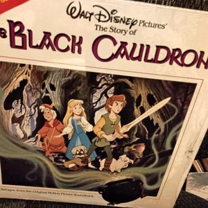 May include: A vintage vinyl record album cover for "The Black Cauldron" from Walt Disney Pictures. The artwork features three animated characters with a sword, a cauldron, and a forest background. The album title is in large, stylized letters.