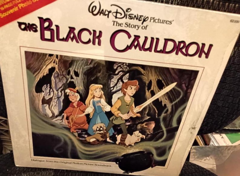 May include: A vintage vinyl record album cover for "The Black Cauldron" from Walt Disney Pictures. The artwork features three animated characters with a sword, a cauldron, and a forest background. The album title is in large, stylized letters.