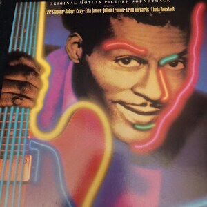 Könnte beinhalten: Ein Vintage-Schallplattencover mit Chuck Berry und dem Titel "Hail! Hail! Rock'N' Roll" sowie den Namen der Musiker Eric Clapton, Robert Cray, Etta James, Julian Lennon, Keith Richards und Linda Ronstadt. Das Bild ist mit Neonfarben und einer Gitarre stilisiert.