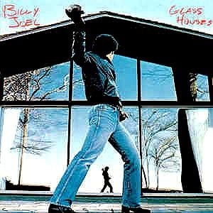 May include: Album cover for Billy Joel's "Glass Houses." The image features a person in a leather jacket and jeans throwing a rock through a window. The album title is in the upper right corner, and the artist's name is in the upper left.