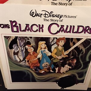May include: A book cover for "The Black Cauldron" featuring a colorful illustration of characters from the Disney film. The title is in large, purple letters. The image shows a young man with a sword, a woman in a blue dress, and other characters.