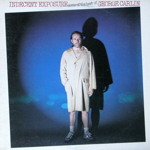 Puede incluir: Un hombre con un abrigo beige claro de gabardina se encuentra de pie frente a un fondo azul. La portada del álbum dice "Indecent Exposure: Some of the Best of George Carlin".