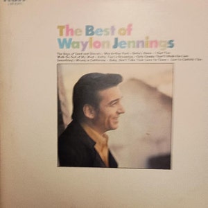 Könnte beinhalten: Ein Vintage-Vinyl-Schallplattencover mit einem Porträt von Waylon Jennings. Der Albumtitel "The Best of Waylon Jennings" ist in bunten Buchstaben gedruckt. Das Albumcover ist weiß mit einem hellbraunen Rand.