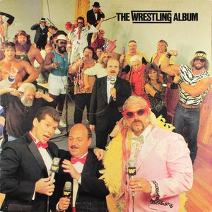 Puede incluir: Un grupo de luchadores, algunos con trajes coloridos, posan para una foto con micrófonos en la mano. El texto "THE WRESTLING ALBUM" está impreso en la parte superior de la imagen.