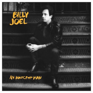 Può includere: Foto in bianco e nero di Billy Joel seduto su una scalinata. Il titolo dell'album "An Innocent Man" è scritto in lettere gialle sotto di lui.