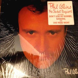 May include: A vinyl record album featuring a close-up of Phil Collins' face with a red-orange hue. The album cover is sealed in plastic and includes a sticker with the album title "No Jacket Required" and song titles.