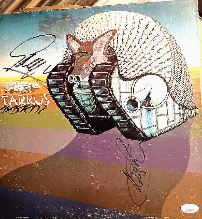 May include: Album cover art featuring a surreal illustration of an armadillo-like creature in a tank. The artwork is signed and includes the text "Tarkus" in a stylized font. The color palette includes blues, browns, and purples.