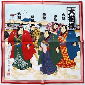 Puede incluir: Un pañuelo cuadrado blanco con un borde rojo que presenta una impresión en bloque de madera japonesa. La impresión representa luchadores de sumo con túnicas coloridas, con texto en caracteres japoneses. Una montaña y un puente están en el fondo.