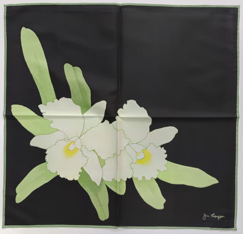 Puede incluir: Pa&ntilde;uelo cuadrado de seda negra con dise&ntilde;o floral. El pa&ntilde;uelo presenta dos orqu&iacute;deas blancas con centros amarillos y hojas verde claro. El borde es verde claro y el pa&ntilde;uelo est&aacute; firmado "Jim Thompson" en la esquina inferior derecha.