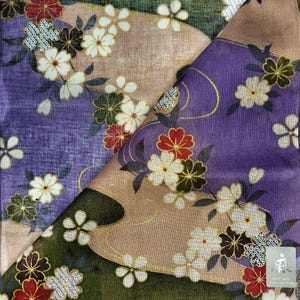 Puede incluir: Primer plano de una tela doblada con un diseño floral. La tela presenta tonos morados, verdes y beige, adornada con flores blancas, rojas y verde oscuro. Los detalles dorados resaltan el diseño, creando una estética detallada y elegante.