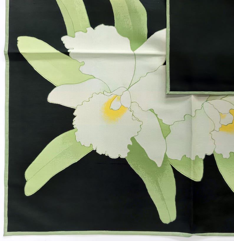 Puede incluir: Pa&ntilde;uelo cuadrado en blanco y negro con un dise&ntilde;o de orqu&iacute;deas. Las orqu&iacute;deas son blancas con centros amarillos y hojas verdes. El pa&ntilde;uelo tiene un borde verde. Mide aproximadamente 60 cm x 60 cm.