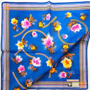 Könnte beinhalten: Blaues quadratisches Taschentuch mit floralem Muster. Das Design zeigt rosa, gelbe und orangefarbene Blumen mit geschwungenen Linien. Der Rand hat Streifen in Weiß, Rosa, Gelb und Blau. Der Text "kansai yamamoto" ist sichtbar.