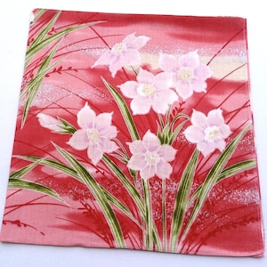 May include: A pink cotton handkerchief with a floral design. The handkerchief features white flowers with green leaves on a pink background with a subtle shimmer.