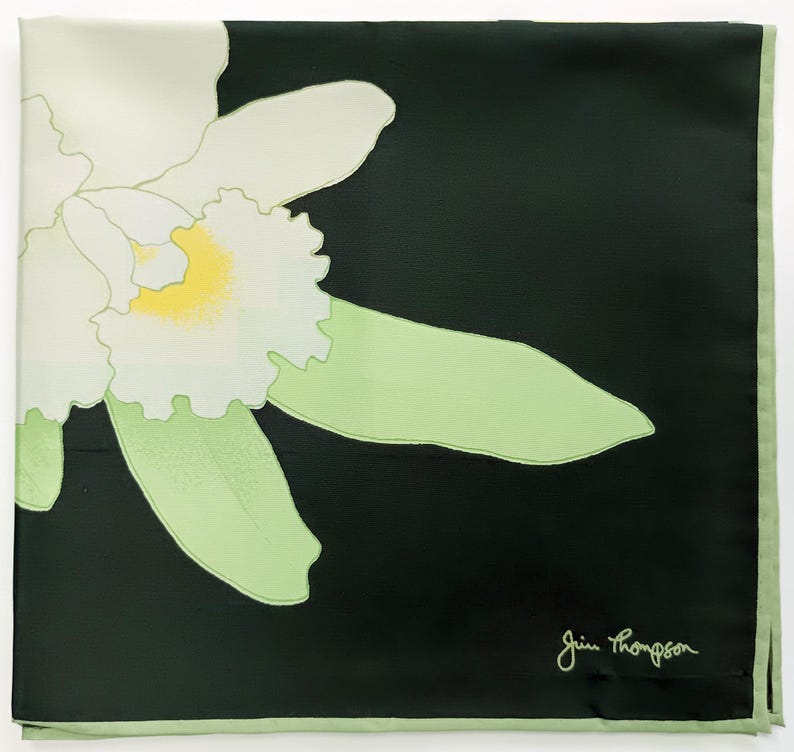 Puede incluir: Pa&ntilde;uelo cuadrado de seda con un gran dise&ntilde;o de orqu&iacute;dea blanca y amarilla sobre fondo negro. La orqu&iacute;dea tiene hojas verde claro y un borde verde claro. La firma "Jim Thompson" est&aacute; en la esquina inferior derecha.