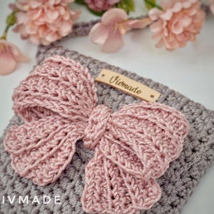 May include: A gray crocheted crossbody bag with a pink crocheted bow and a wooden tag that says "Vivmade".