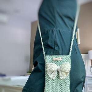 May include: A light green crocheted crossbody bag with a white crocheted bow. The bag has a small label that says "remarkable".