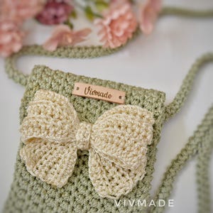 May include: A green crocheted bag with a white crocheted bow and a wooden tag that says "Vivmade".